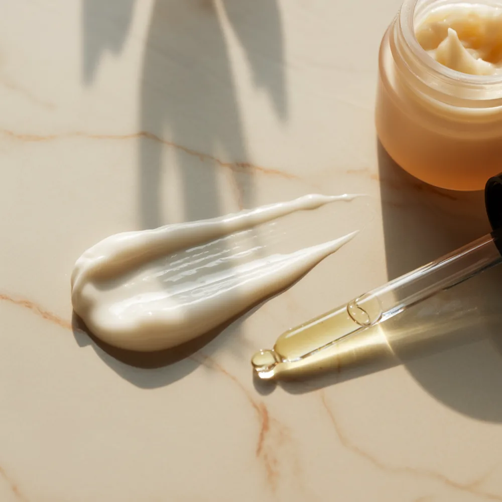 Close up of a glossy serum smear next to a thick white moisturizer smear on marble