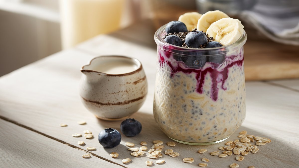 Overnight oats without yogurt, creamy and dairy-free, topped with fresh fruit A glass jar of creamy overnight oats topped with blueberries and banana with almond milk and oats nearby